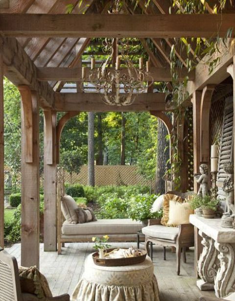 a neutral rustic meets vintage terrace with vintage neutral furniture, a console table and a coffee table with a cover, a chic chandelier and potted greenery
