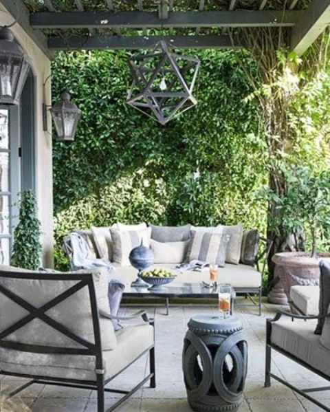 a vintage neutral terrace with metal furniture, grey upholstery, side tables, a creative geometric pendant lamp and greenery