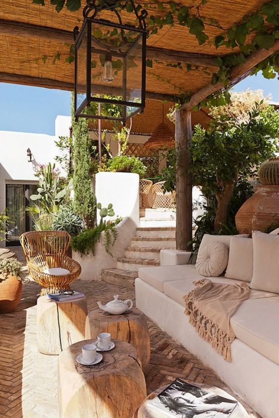 a rustic neutral terrace with a large sofa, tree stump coffee tables, greenery and blooms around feels rather Mediterranean