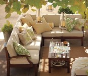 a modern neutral terrace with a corner sofa, a low coffee table, neutral and printed pillows and greenery over the space