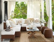 a small and cozy neutral terrace with brown wicker furniture with white upholstery, a coffee table and neutral curtains around