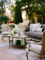 a refined neutral terrace with vintage furniture with neutral upholstery, a tiered glass coffee table and white blooms