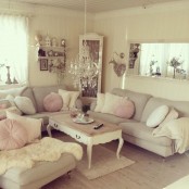 a neutral shabby chic living room with a grey sectional, white and pink pillows, a crystal chandelier and lots of pretty accessories
