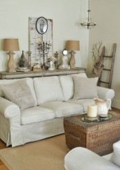 a neutral shabby chic living room with simple and rustic furniture, a woven chest, some table lamps and decor and vintage shutters