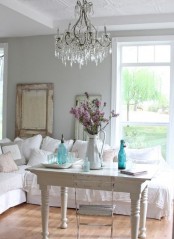 a white shabby chic living room with vintage furniture, a crystal chandelier, blue vases, blooms and a mirror