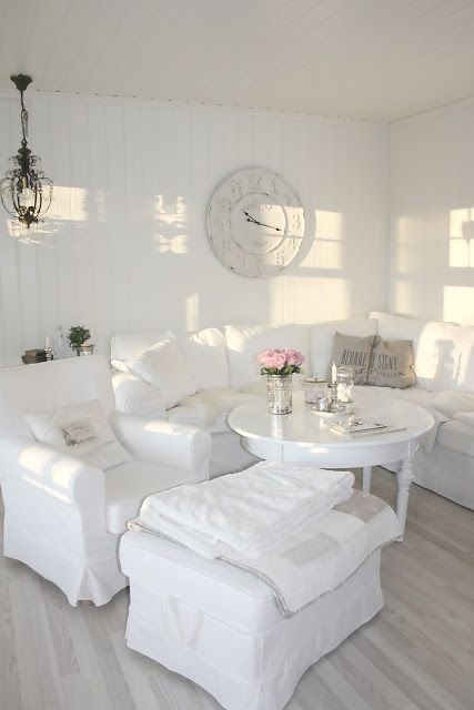 a white shabby chic living room with refined furniture, a white table, a clock and a crystal chandelier is very elegant