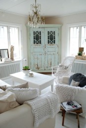 a shabby chic living room in neutrals, with a mint cabinet, a crystal chandelier, crochet and knit blankets and pillows