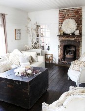 a shabby chic living room in neutrals, with a brick fireplace, a dark chest table, neutral textiles and pillows seems cozy and welcoming