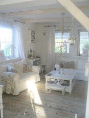 a white shabby chic living room with vintage furniture, wooden beams, a crystal chandelier, lace and white plain curtains