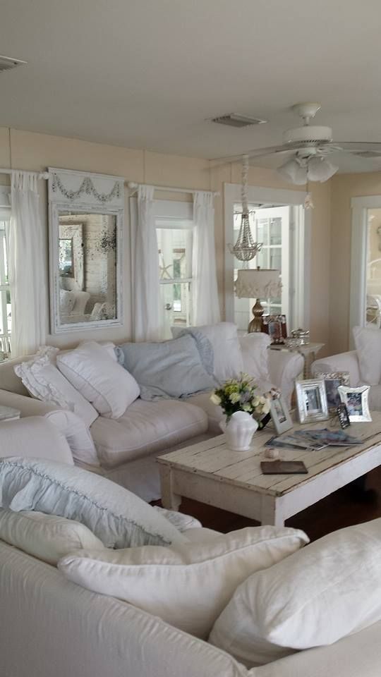 a neutral shabby chic living room with warm-colored walls, neutral furniture and pillows, a beaded chandelier and pastel touches here and there