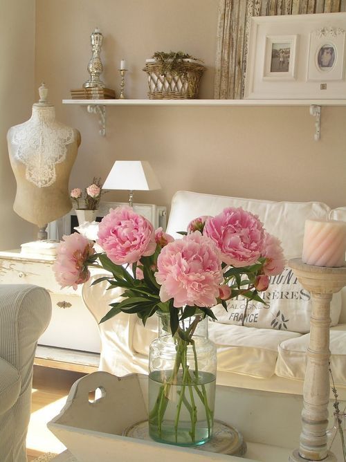 a romantic shabby chic living room in neutrals, with simple and elegant furniture, an open shelf, some art and candles and blooms