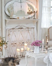 a white shabby chic living room with a non-working fireplace covered with a screen, an oval mirror and refined furniture
