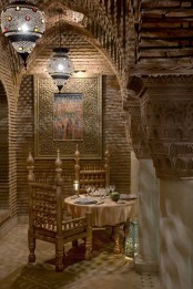 a neutral Moroccan dining space with stone walls, arches, a wooden carved table and chairs and catchy Moroccan pendant lamps