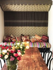 a stylish Moroccan dining room with a wooden table and black chairs, a bright upholstered bench and a bold tapestry over the bench
