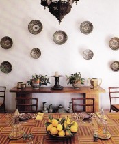 a Moroccan dining room with light stained wooden furniture, decorative plates on the wall, Moroccan lanterns and lamps on the table
