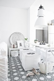 a neutral Moroccan dining room with a printed tile floor, white furniture and printed poufs, a chic plate for decor and potted plants
