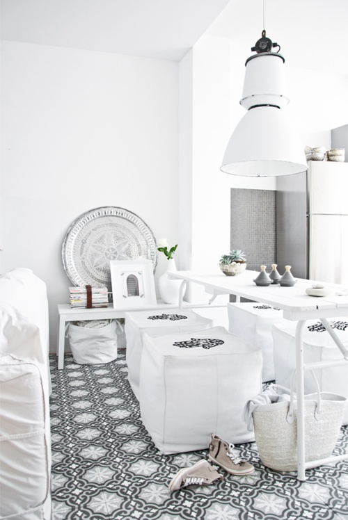 a neutral Moroccan dining room with a printed tile floor, white furniture and printed poufs, a chic plate for decor and potted plants