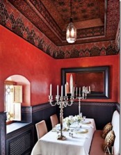 a bright Moroccan dining room with navy and red walls, a painted ceiling, a neutral table and a chic upholstered bench plus a pendant lamp