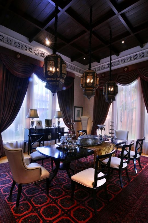 a refined Moroccan dining space with a black table and pretty upholstered chairs, pendant lamps that create a mood and dark textiles and a cool ceiling
