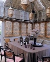 a neutral Moroccan dining space with a table covered with a mauve tablecloth, printed chairs, Moroccan lanterns on the table and over the space and neutral printed textiles
