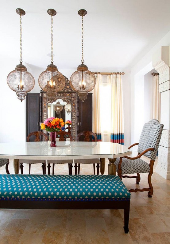 a bright dining room with a pretty white table, a bright upholstered bench and a chair, chic pendant lamps over the table and colorful textiles