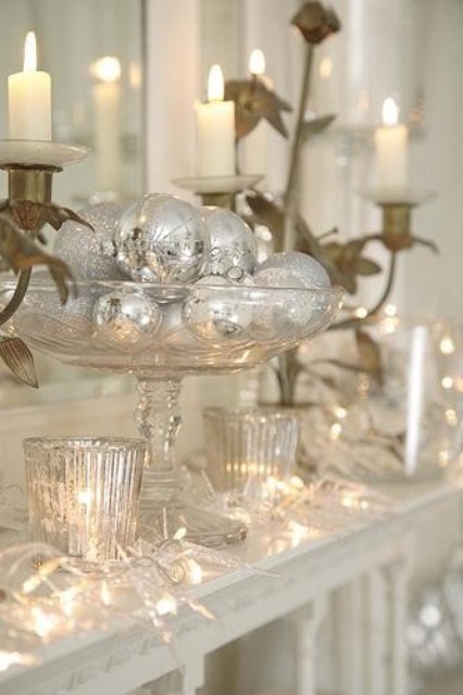 a beautiful Christmas mantel with lights, candles, a glass stand with silver ornaments and giled candelholders is amazing
