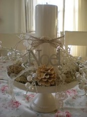a vintage white Christmas centerpiece of a stand with hay, a pillar candle, berries, white lace and bleached pinecones is an amazing idea for Christmas