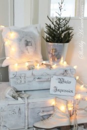 dreamy white Christmas decor with vintage suitcases, skates, pillows, a mini tree in a bucket and lights is beautiful