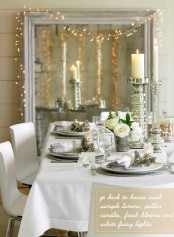 a refined vintage white and silver Christmas tablescape with tall mercury glass candleholders, silver chargers and white porcelain, a white floral centerpiece