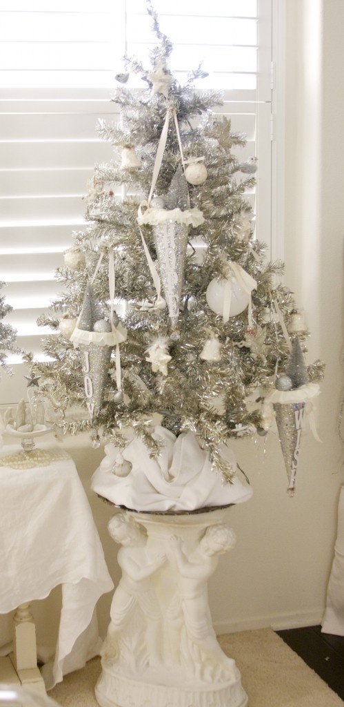 a silver Christmas tree decorated with white baubles and stars and oversized silver cones with the same ornaments is wow