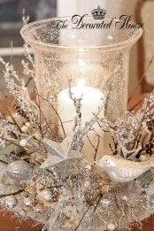 a refined and chic Christmas centerpiece of silver branches, stars and beads that surround a snowy candleholder with a pillar candle