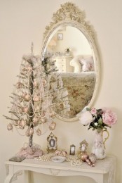 exquisite white vintage Christmas decor with a mirror in an ornated frame, a silver mini tree with white bead garlands and pink ornaments, pearls and blooms