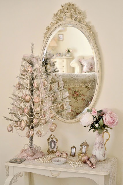 exquisite white vintage Christmas decor with a mirror in an ornated frame, a silver mini tree with white bead garlands and pink ornaments, pearls and blooms