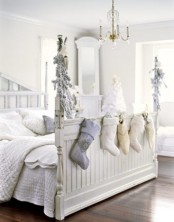 an all-white vintage bedroom with a planked bed decorated with neutral stockings and neutral evergreens, a vintage white chandelier