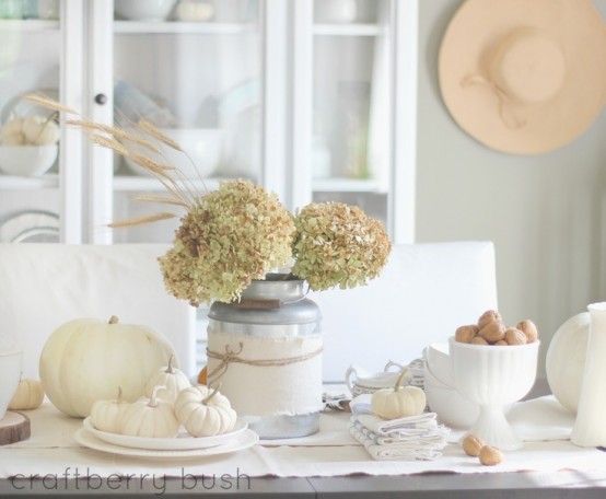 a white and neutral fall tablescape with a white table runner, white pumpkins, nuts in a bowl and neutrla hydrangeas for the fall