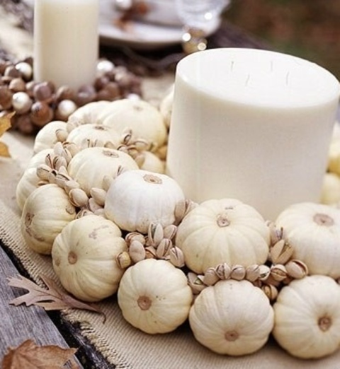 a white fall centerpiece of a giant pillar candle and white pumpkins and pistachios is a creative and all-natural idea