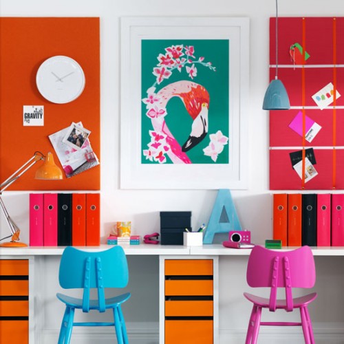 a colorful shared home office with orange walls, a long desk with orange drawers, blue and pink chairs, a bold artwork is a super bold space to get inspiration from