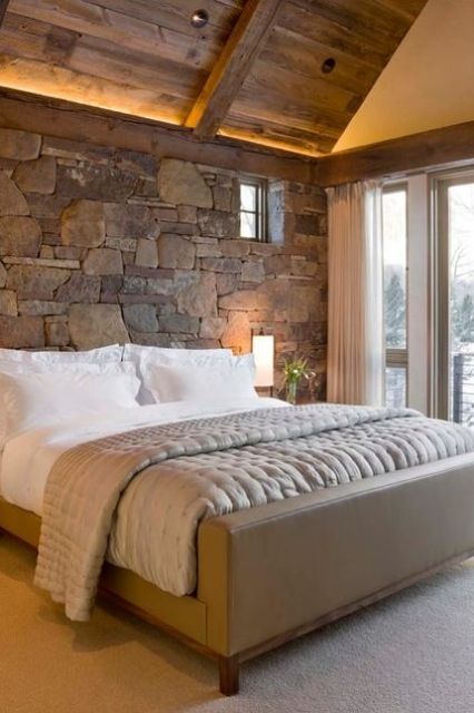 a real stone wall in various shades plus a wooden ceiling is a great idea for a catchy chalet bedroom
