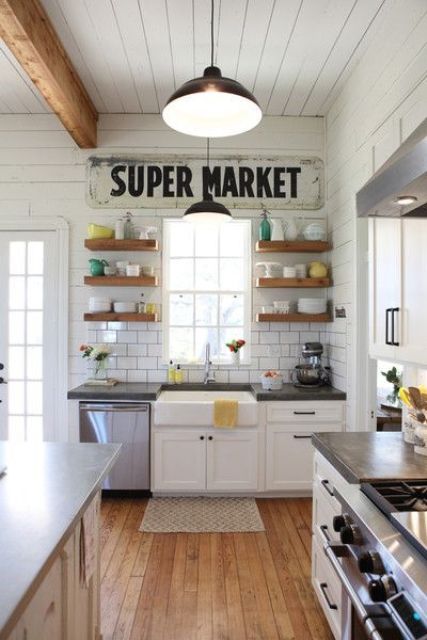 a pretty white vintage kitchen with white cabinets, black countertops, open shelves, pendant lamps and a wooden kitchen island