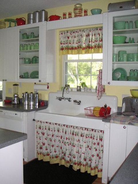 a vintage kitchen with white cabinets, glass and usual ones, yellow walls, touches of green and red and floral textiles