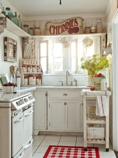 a pretty vintage kitchen in white, with chic cabinets, a long open shelf for storage, a tiny cart as a kitchen island and touches of red and mint green
