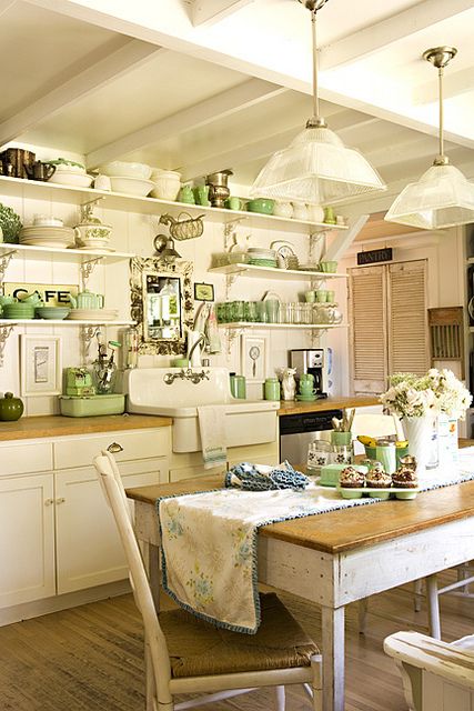 a neutral vintage kitchen with cabinets, open shelves, butcherblock countertops, a table and chairs, green tableware and cookware