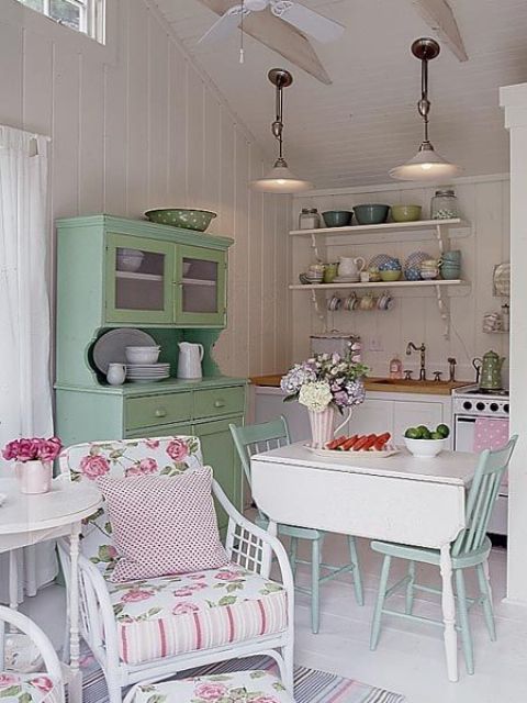 a neutral vintage kitchen with built-in cabinets, a green buffet, a folding table and blue chairs, colored tableware and chairs with floral upholstery