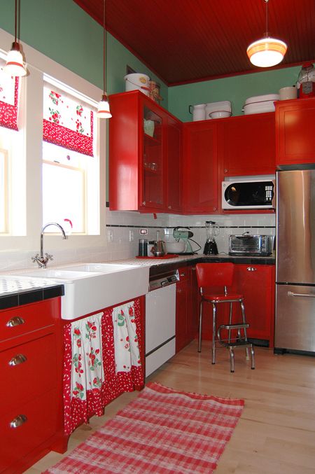 a vintage kitchen with green walls, red cabinets, usual and glass ones, a tiled countertop and some floral and fruit prints