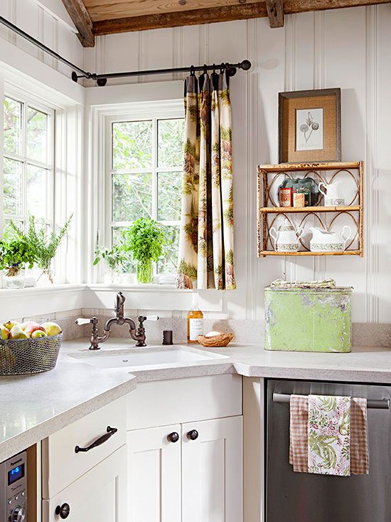 a chic vintage kitchen with white cabinets, white stone countertops, potted greenery, a lovely shelf, printed textiles