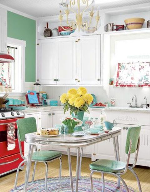 a vintage kitchen with white cabinets, a hot red cooker, green chairs and a green accent wall plus floral touches and a vintage chandelier