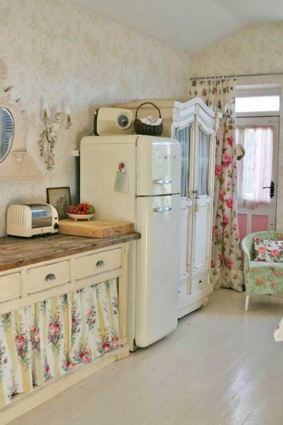 a cute vintage and shabby chic kitchen with white cabinets, a green floral chair and other textules, butcherblock countertops and vintage accessories