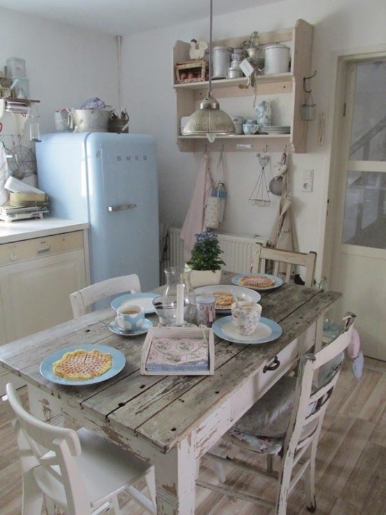 a vintage and shabby chic neutral kitchen with neutral cabinets, a blue fridge, a shabby chic wooden dining set, open shelves and touches of blue and blush