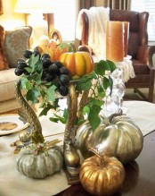 an elegant metal stand with greenery, fresh grapes, fall leaves and bright and metallic faux pumpkins plus candles