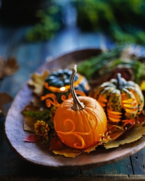 a bowl with fall leaves, blooms and candle lanterns made of little pumpkins is a cool centerpiece or decoration